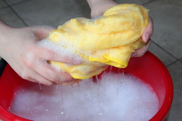 Hands wringing a cloth over a bucket of soapy water