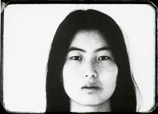 黑白影像中的 Theresa Hak Kyung Cha 直视镜头,画面带有胶片边框和颗粒