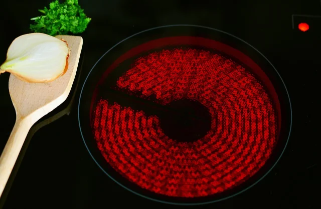 A glowing ceramic hob beside a cutting board and onion