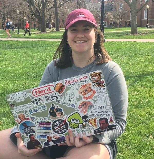 A woman with a laptop sitting on grass in front of a college campus — one of five contractors who found AI training work through Outlier