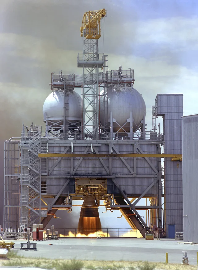 An F-1 engine firing on a test stand, with propellant spheres on the structure above it