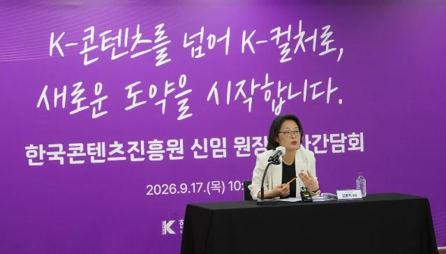 一位短发戴眼镜的女性在记者会上手持麦克风发言,身后是紫色背景板与机构标识