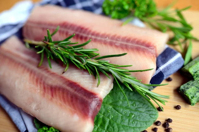 Raw salmon fillets on a wooden board with herbs and peppercorns