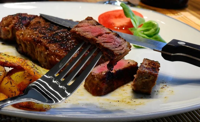 Steak cut into slices on a plate, pink in the middle, with a knife and fork