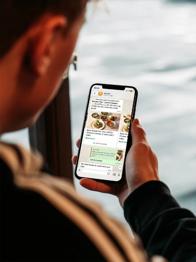 用户手持手机,屏幕为 Just Eat 在 WhatsApp 内的对话,推荐餐厅套餐并给出加购按钮