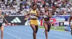 Three women athletes race on a blue track at the Doha Diamond League, the center runner in a yellow kit with Adidas branding visible in the background
