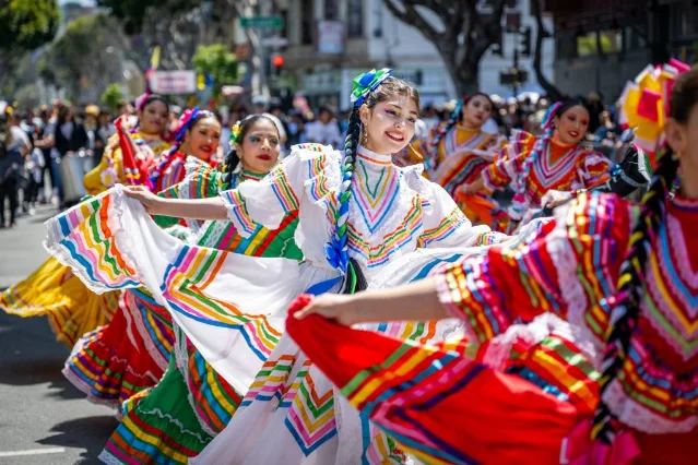 Dancers in vivid folk costumes parade down a Mission District street at Carnaval SF
