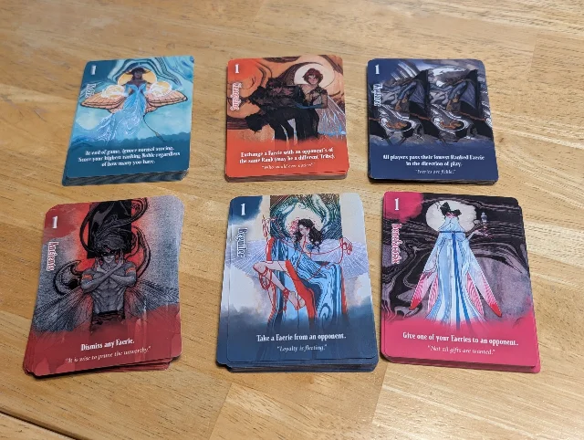 Six coloured Devious faerie decks arranged on a wooden table