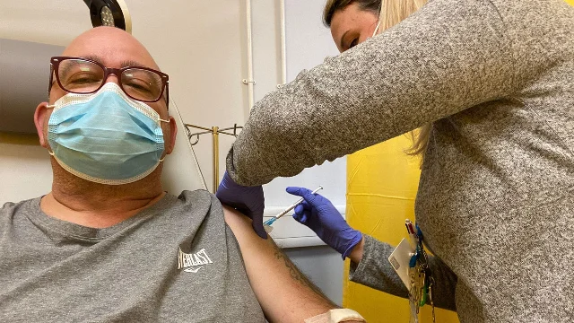A clinician administers a COVID-19 vaccine to an older male patient