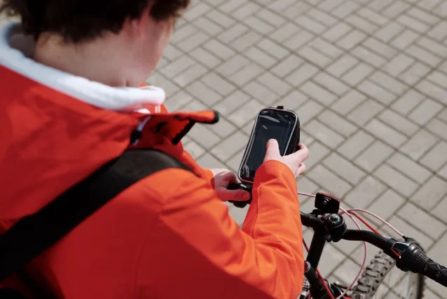 Cyclist setting up phone on bike handlebar mount for navigation, urban street setting