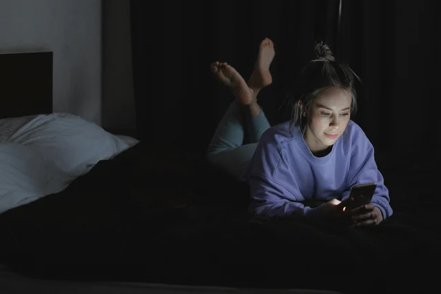 A woman lies in bed at night, scrolling through her phone