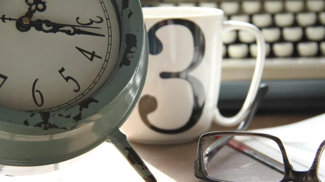 Clock and coffee beside a work desk
