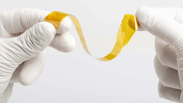 Precision Neuroscience's Layer 7 Cortical Interface held by gloved hands -- a thin flexible electrode array resembling amber tape