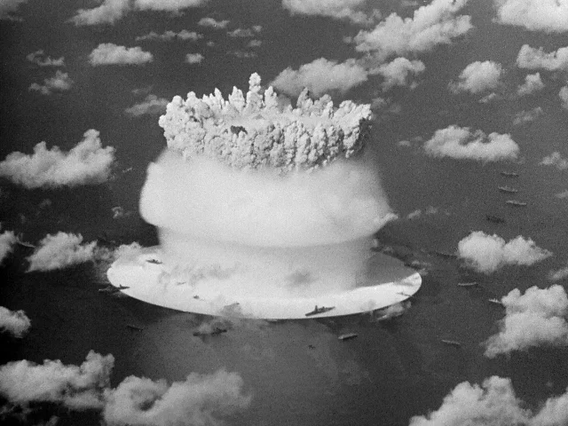 海面上升起巨大的黑白核爆云团,周围散着云层和船只