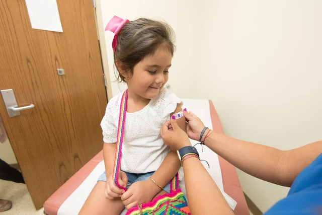 A young girl receives a vaccination at a clinic, with a cheerful expression after getting a band-aid