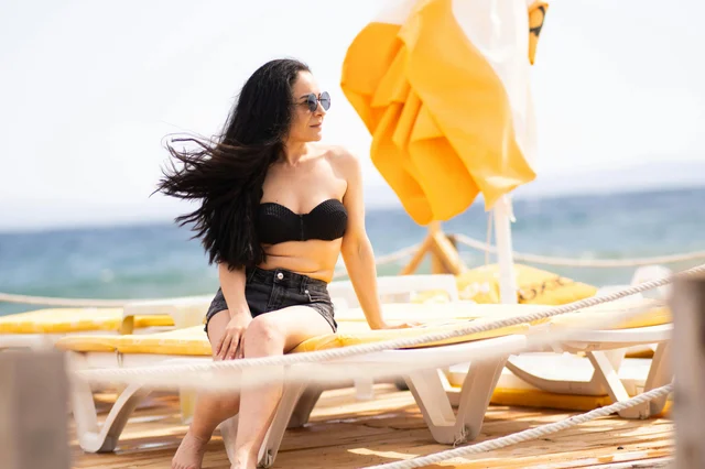 Woman in a bikini relaxing on a sunny beach lounger with the sea in the background