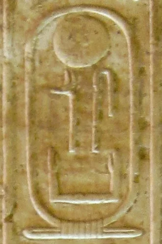 A carved oval name-ring in warm yellow stone, holding hieroglyph signs with a sun disk at the top