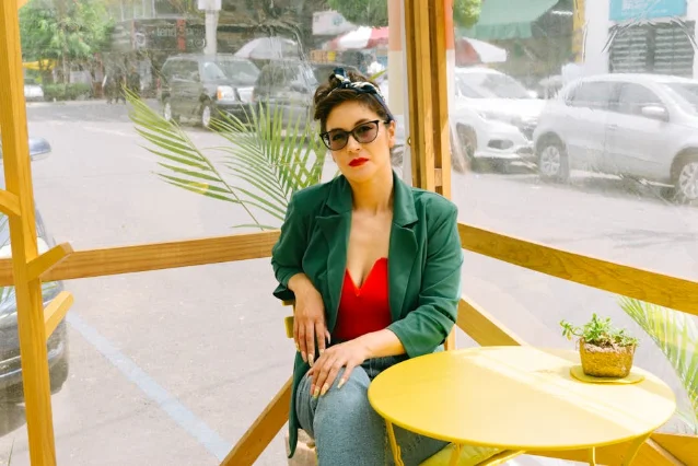 Woman in green blazer and red top at outdoor café, styled confidently
