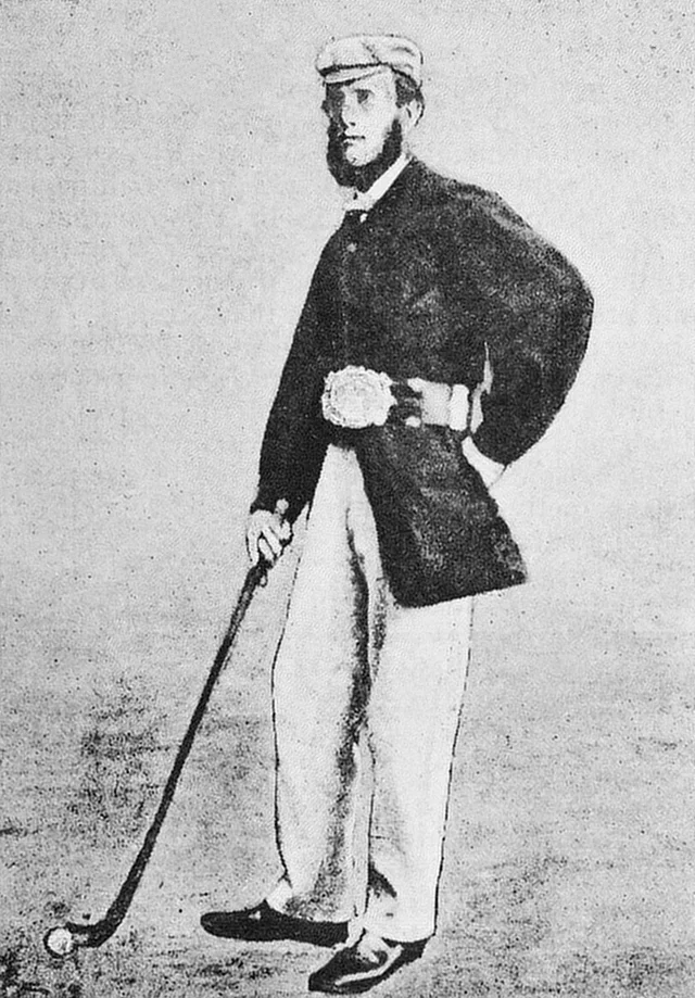 Willie Park Sr. in a dark coat and cap, standing with a wooden club, a large silver-buckled belt around his waist