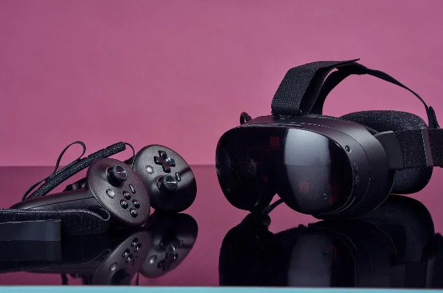 A black Valve Steam Frame headset and its two controllers on a pink studio backdrop