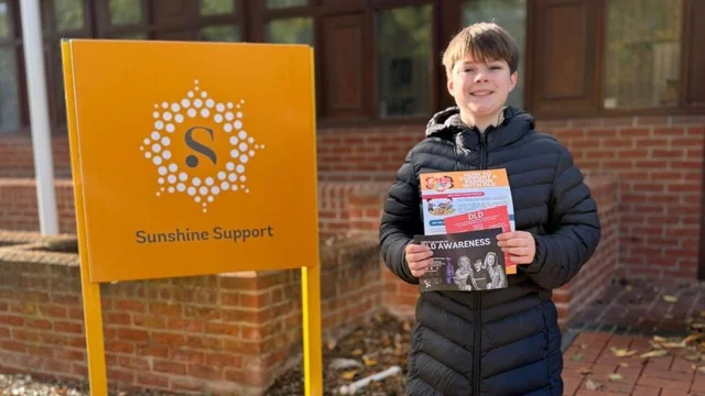 a girl in a black puffer jacket holding leaflets beside a yellow sign