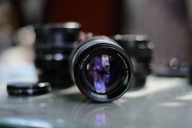 Close-up of a Carl Zeiss Tele-Tessar camera lens showing aperture blades, with blurred background — representing the optical DOF mechanism that SDXL and Flux replicate with training-data bias rather than physics
