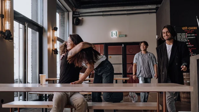 People greeting and hugging in a bar, capturing the energy of Bumble Plans' paid IRL group-dating events