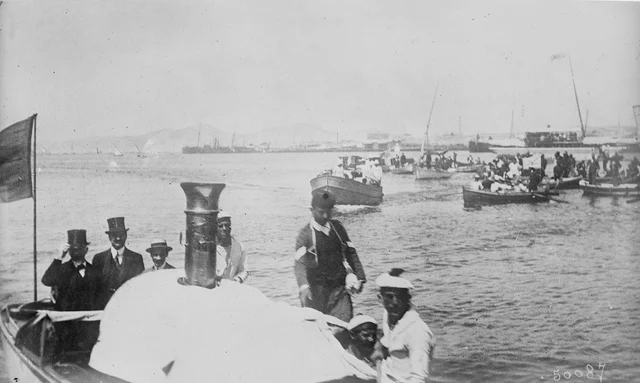 A launch carrying top-hatted men across a harbour crowded with small boats