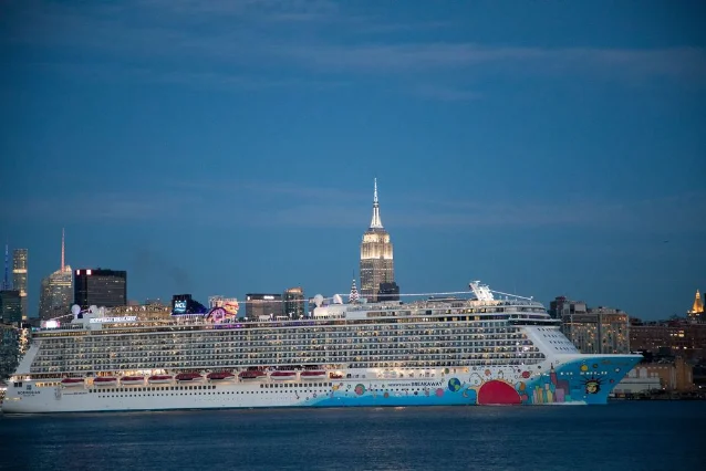Norwegian Breakaway cruise ship docked in New York Harbor with the Manhattan skyline at dusk