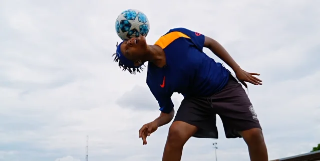 A freestyle footballer balances a ball on her head outdoors