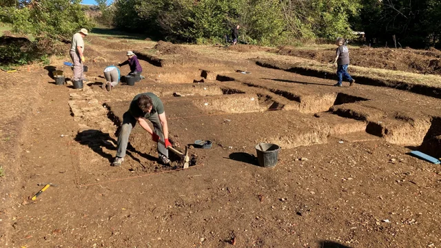 people working with mattocks and buckets across a wide area of opened trenches in a field