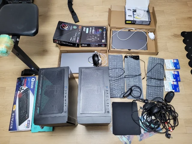 摆放在木地板上的两台黑色电脑主机、主板包装盒、显卡包装盒、键盘与线材