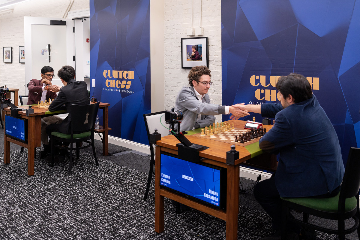 Four players at two boards in a small room, with the Clutch Chess backdrop behind them