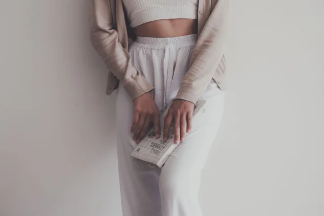 White ribbed crop top with wide-leg ivory trousers and beige cardigan layer, minimal interior setting