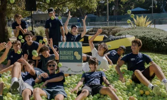 Teenagers from Another Bounce celebrating on top of a pile of thousands of green pickleballs and tennis balls at Reed Park