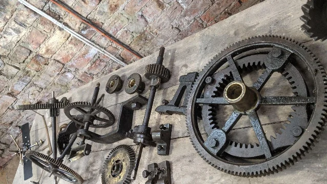 The clock mechanism taken apart and laid out in its individual pieces on a wooden plank