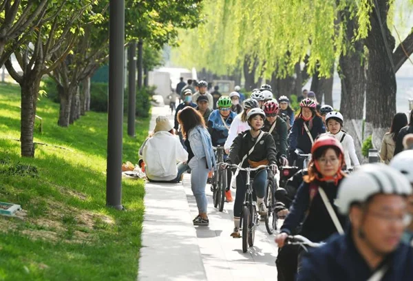 骑行者沿着亮马河畔林荫步道骑行,步道旁垂柳成行,亲水平台上市民休憩