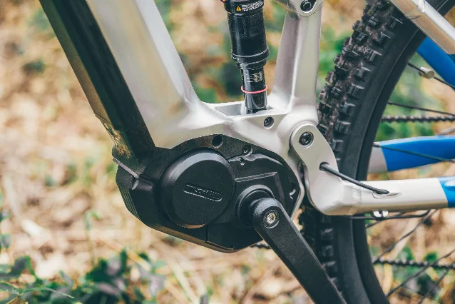 A black fat-tire eBike with a visible mid-drive motor unit in a forest setting