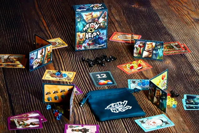 Meow Heist cat cards, gems, and cloth bag mid-round on a wooden table.