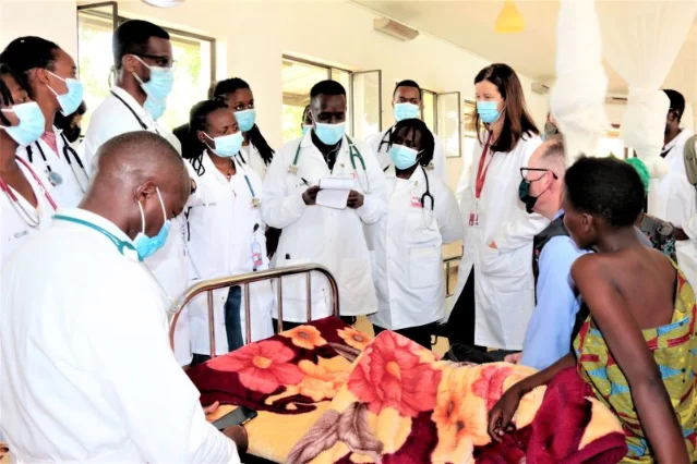 Medical staff in masks and white coats stand around a hospital bed during teaching rounds
