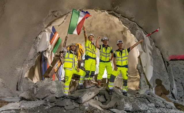 Workers in high-visibility gear celebrating at the breakthrough point of the Brenner Base Tunnel exploratory bore, with Italian and Austrian national flags