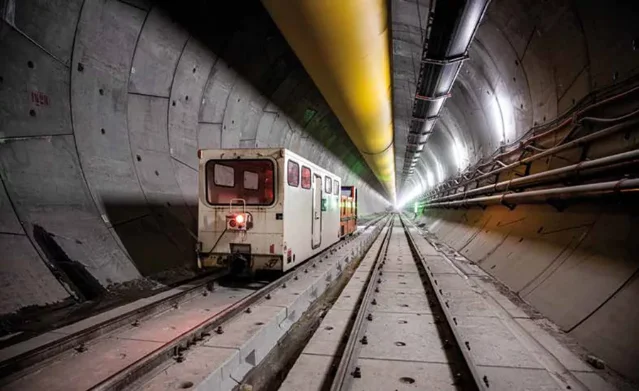 Construction rail vehicles inside the Brenner Base Tunnel exploratory bore — segmental concrete ring lining, ventilation ducting, and service rails visible