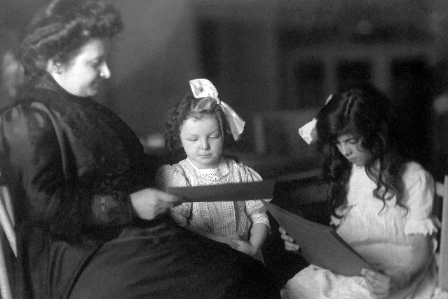 Maria Montessori, left, seated with two children holding letter cards