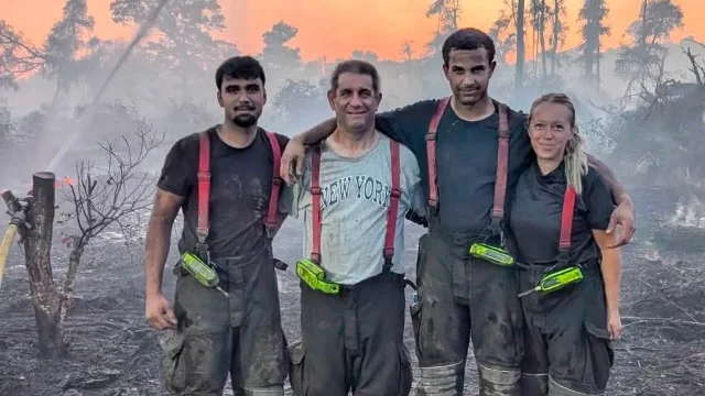Four members of Peterborough Volunteer Fire Brigade stand together at a smoky, burned woodland site.