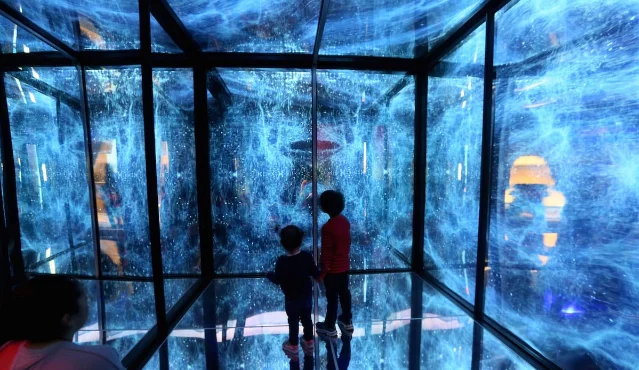 Children standing inside Iyvone Khoo's Infinity Cube, its mirrored walls filled with projected blue-white light