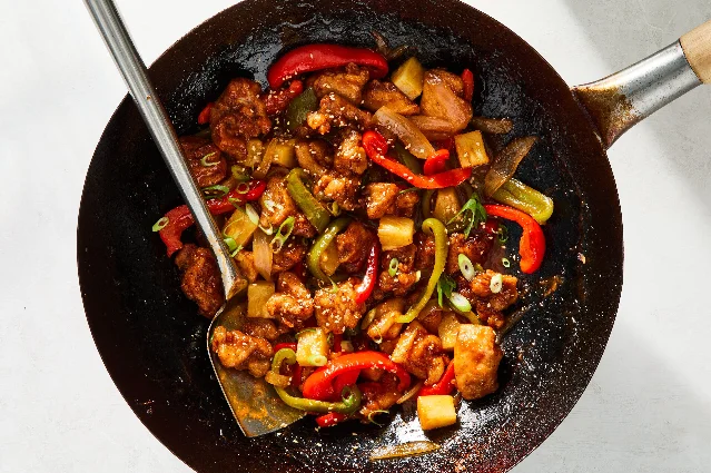 Sweet-and-sour chicken with peppers, onion, pineapple and scallions in a black wok