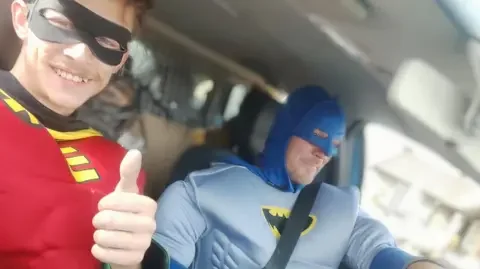 Liam Keen and Dennis Rawlings, dressed as Batman and Robin, prepare to head out in a van.