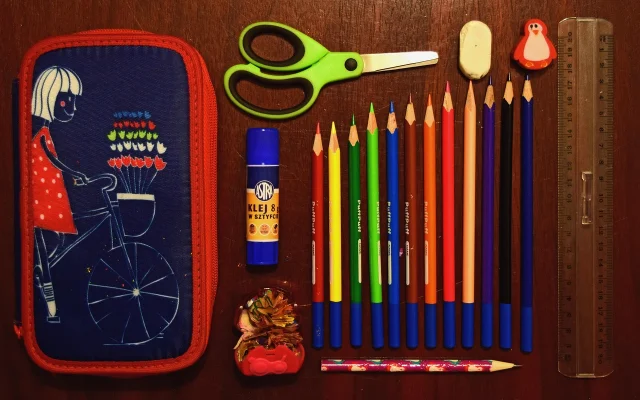 Flat lay of an organized pencil case containing pens, pencils, ruler, eraser, and glue stick on a wooden surface