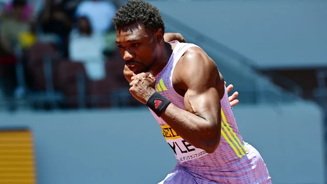 Noah Lyles mid-race at the 100m in Rome, bib visible, in full stride against a blue track backdrop