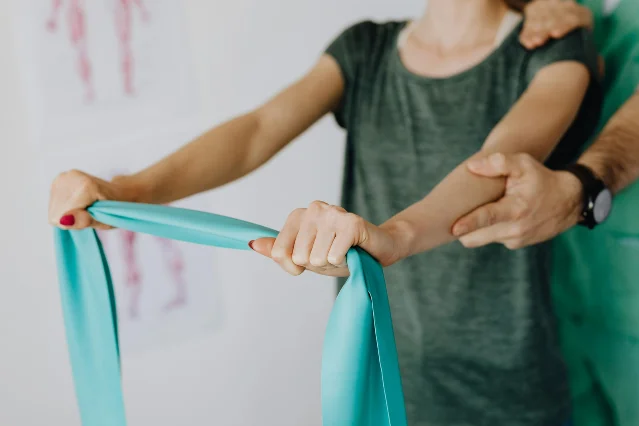 Physical therapist supporting a patient's shoulder with a resistance band during rehabilitation